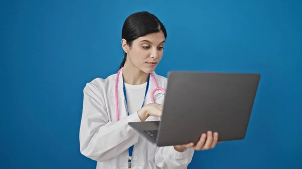 年轻美丽的惊慌失措的女医生用笔记本电脑站在孤立的蓝色背景上 — 图库照片