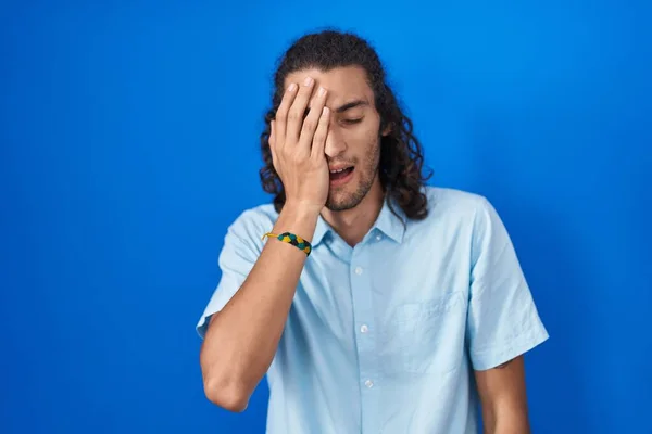 Mladý Hispánec Stojící Nad Modrým Pozadím Unaveně Zírající Zakrývající Napůl — Stock fotografie