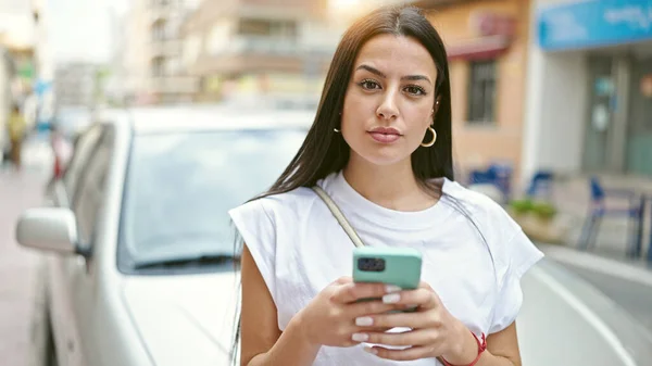 stock image Young beautiful hispanic woman using smartphone standing by car at street