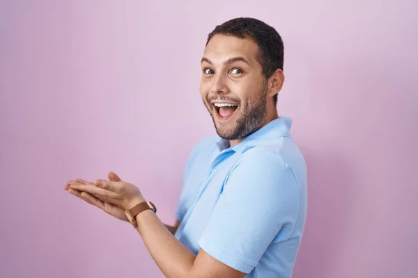 ヒスパニック系の男立って上ピンクの背景指摘脇に手オープンヤシショーコピースペース 提示広告笑顔興奮幸せな — ストック写真