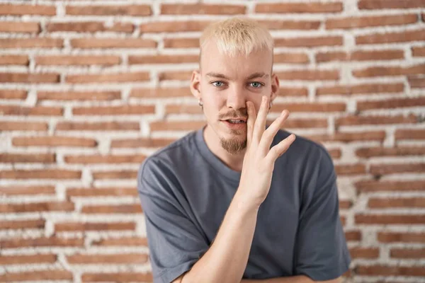口の上にレンガの壁の手の上に立っている若い白人男性は 悪意のある話の会話をささやく — ストック写真