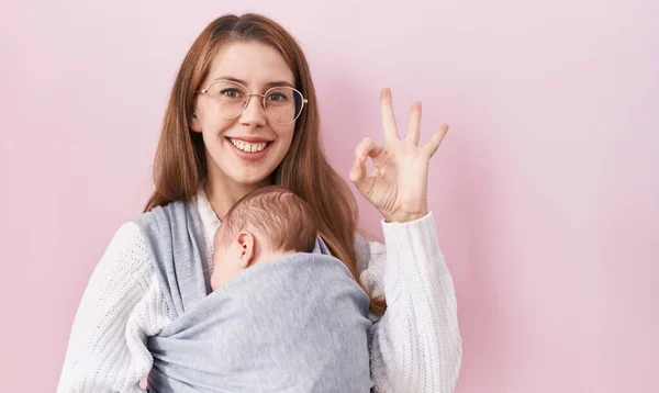Kucağında Bebek Taşıyan Beyaz Bir Kadın Parmaklarıyla Işareti Yapıyor Gülümseyerek — Stok fotoğraf