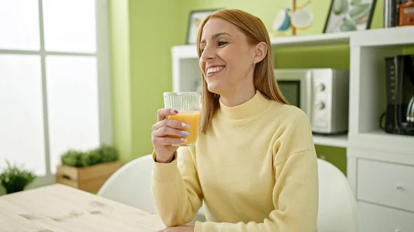年轻的金发女人坐在家里的桌上喝橙汁 — 图库照片