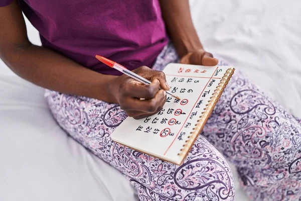 在日历上书写的非裔美国妇女坐在床上卧室里 — 图库照片
