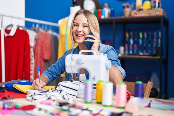 Young Blonde Woman Tailor Talking Smartphone Writing Notebook Sewing Studio — 스톡 사진