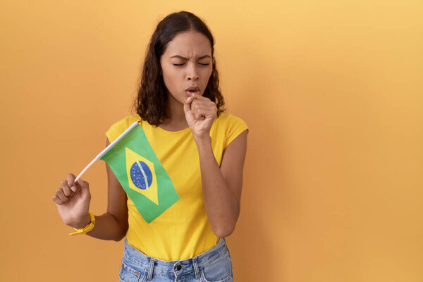 Young hispanic woman holding brazil flag feeling unwell and coughing as symptom for cold or bronchitis. health care concept. 