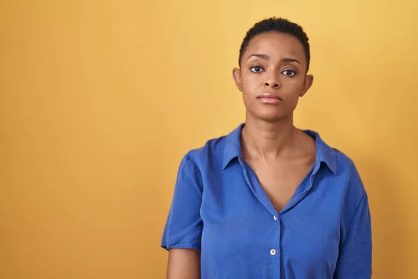 站在黄色背景上的非洲裔美国妇女面带严肃的表情放松了下来 简单而自然地看着相机 — 图库照片
