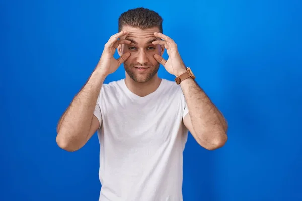 Young Caucasian Man Standing Blue Background Trying Open Eyes Fingers — Stock Photo, Image