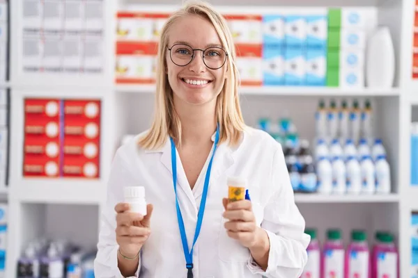 Joven Mujer Rubia Farmacéutica Sonriendo Confiado Sosteniendo Pastillas Botellas Farmacia — Foto de Stock