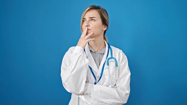 Genç Sarışın Kadın Doktor Şüpheli Bir Ifadeyle Dikiliyor Mavi Arka — Stok fotoğraf