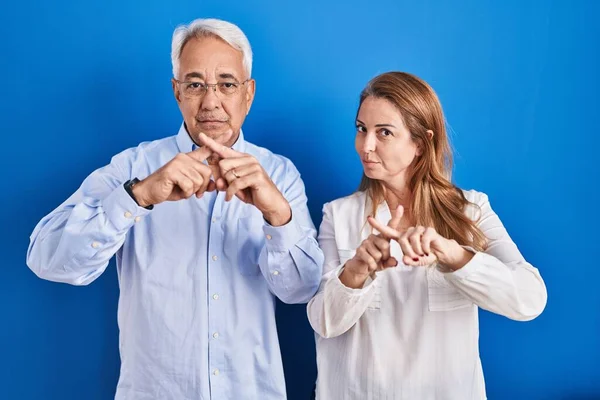 中年时 他的一对惊慌失措的夫妇站在蓝色背景下 用手指交叉表示拒绝 做阴性手势 — 图库照片