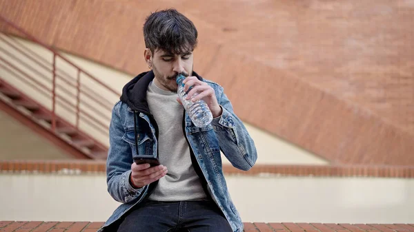 Joven Hispano Sentado Bebiendo Agua Usando Smartphone Calle — Foto de Stock
