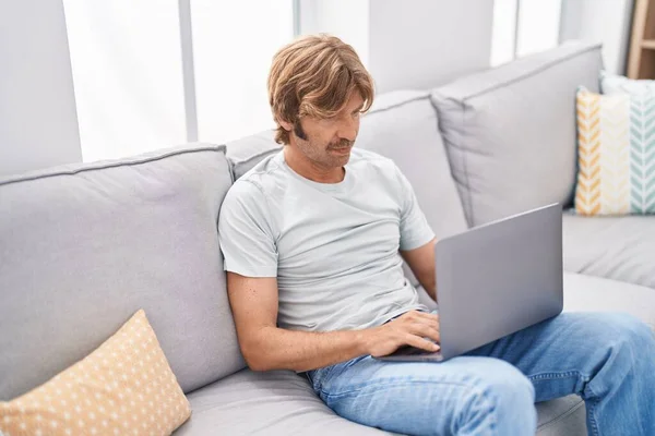 使用笔记本电脑坐在家里的沙发上的年轻人 — 图库照片