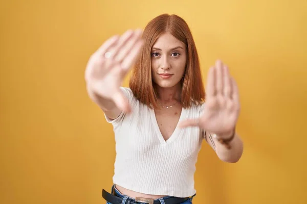 年轻的红头发女人站在黄色的背景上 用手心和手指 相机的视角做着画框 — 图库照片