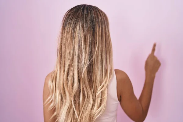 年轻的金发女子站在粉色的背景上 手指头朝前看去 倒立着 — 图库照片