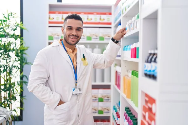 Jovem Hispânico Homem Farmacêutico Sorrindo Confiante Segurando Produto Prateleira Farmácia — Fotografia de Stock