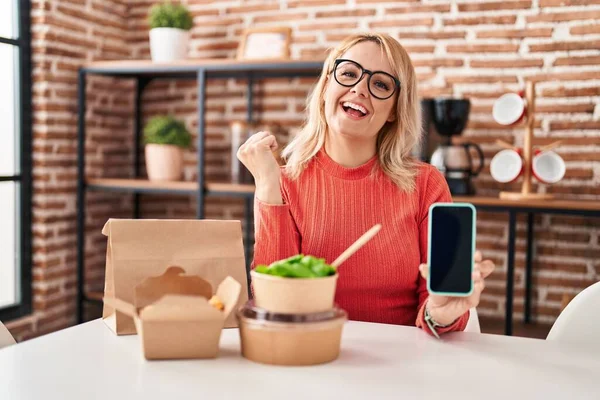 Blonde Frau Isst Essen Zum Mitnehmen Und Zeigt Smartphone Bildschirm — Stockfoto