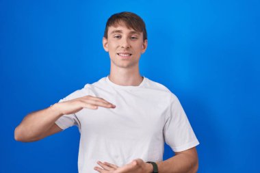 Beyaz, sarışın bir adam mavi arka planda duruyor. Ellerinde büyük ve büyük bir işaret var. Ölçü sembolü. Kameraya bakıp gülümsüyor. ölçüm kavramı. 