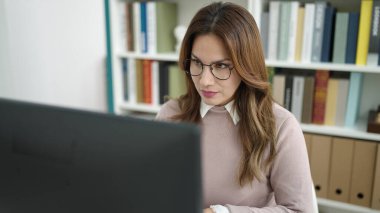 Young beautiful hispanic woman student using computer studying at library university