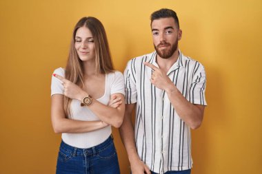 Sarı arka planda duran genç bir çift el ile işaret ederek reklamlarını gösteriyor, ciddi ve sakin bir yüz. 