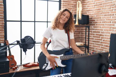 Genç, güzel, İspanyol bir müzisyen müzik stüdyosunda gitar çalarken gülümsüyor.