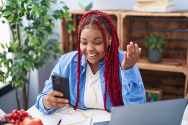 Saçlarını ördürmüş, akıllı telefon kullanan Afro-Amerikalı kadın başarıyı mutlu bir gülümsemeyle ve elini kaldırarak kutluyor. 