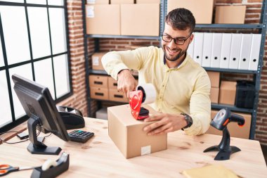 Young hispanic man ecommerce business worker packing cardboard box at office