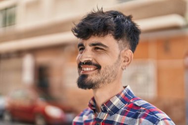 Young hispanic man smiling confident looking to the side at street
