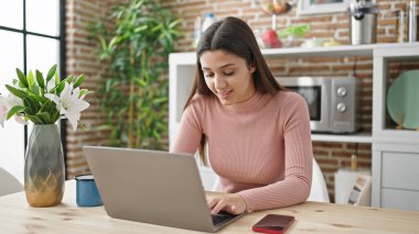 Yemek odasındaki masada dizüstü bilgisayar kullanan güzel İspanyol kadın.