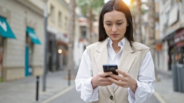 Genç ve güzel İspanyol kadın akıllı telefon kullanıyor. Sokakta ciddi bir ifadesi var.