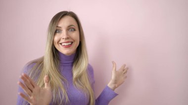 Young blonde woman standing with surprise expression over isolated pink background