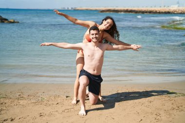 Young hispanic couple tourists wearing swimsuit standing with arms open at seaside