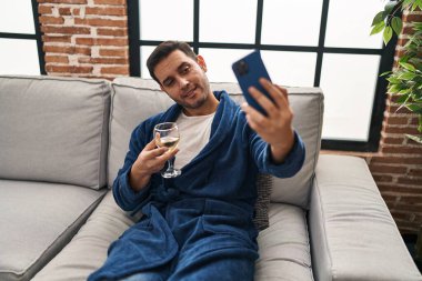 Genç İspanyol adam akıllı telefonla özçekim yapıyor. Evde şarap içiyor.