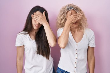 Anne ve kızı pembe arka planda birlikte duruyorlar. Gözleri kapatıyorlar, ciddi ve üzgün görünüyorlar. Görme, saklama ve reddetme konsepti 