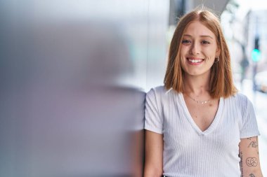 Caddede kendine güvenen genç kızıl saçlı kadın gülümsüyor