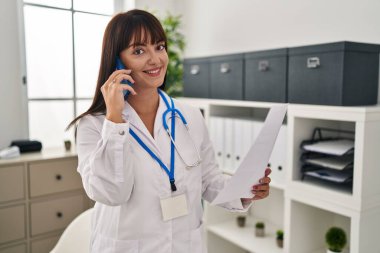 Genç, güzel İspanyol kadın doktor klinikte akıllı telefon okuyarak konuşuyor.