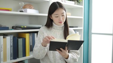 Young chinese woman student reading book studying at library university