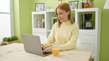 Young blonde woman using laptop having breakfast at home
