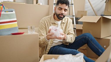 Young hispanic man packing cardboard box at new home