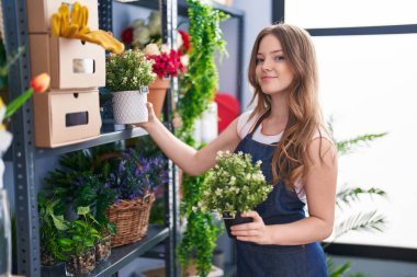 Young woman florist smiling confident holding plant at florist shop