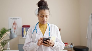 Genç Afrikalı Amerikalı kadın doktor klinikte akıllı telefon kullanıyor.