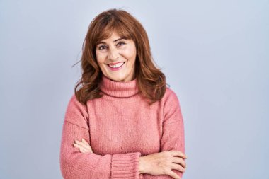 Orta yaşlı İspanyol kadın izole edilmiş arka planda durmuş kollarını kavuşturup kameraya bakarken gülümsüyor. pozitif kişi. 