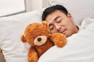 Young chinese man lying on bed sleeping with teddy bear at bedroom