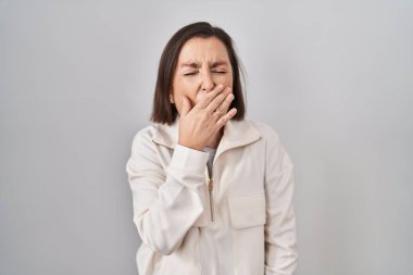 Orta yaşlı İspanyol kadın izole edilmiş arka planda dikiliyor. Elle ağzını kapatmaktan sıkılmış. Huzursuz ve uykulu.. 
