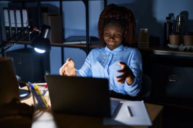 Geceleri ofiste çalışan Afrikalı kadın kameraya sarılıp gülümseyerek gülümsüyor. Mutluluğu kucaklayan neşeli bir ifade.. 