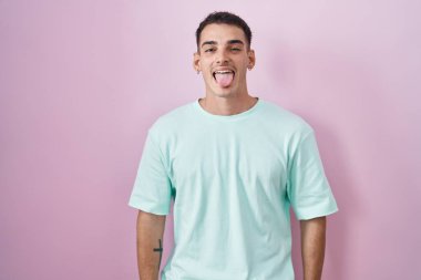 Pembe arka planda duran yakışıklı İspanyol adam komik bir ifadeyle dilini dışarı çıkarıyor. duygu kavramı. 