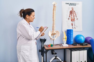Orta yaşlı İspanyol kadın fizyoterapist rehabilitasyon kliniğinde omurganın anatomik modelini gösteriyor.