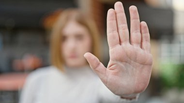 Young blonde woman doing stop gesture with hand at coffee shop terrace