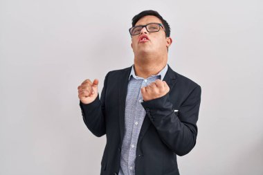 Down sendromlu genç İspanyol adam iş stili giyiniyor. Çok mutlu ve heyecanlı. Kolları havada, gülümsüyor ve başarı için bağırıyor. kutlama konsepti. 