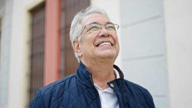 Orta yaşlı, gri saçlı, kendine güvenen bir adam caddeye bakıyor.